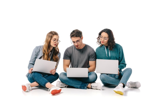Drei multikulturelle Studenten, die mit Laptops auf Weiß sitzen