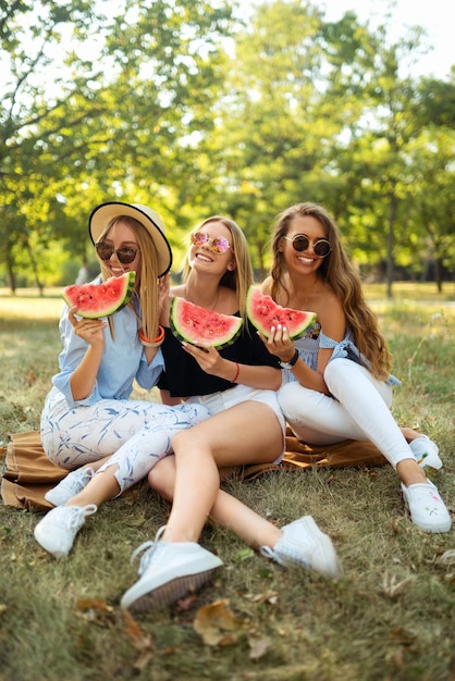 Drei nette Mädchen, die Spaß haben, Wassermelone im Park zu essen Ausgezeichnetes sonniges Wetter Schöne Figuren