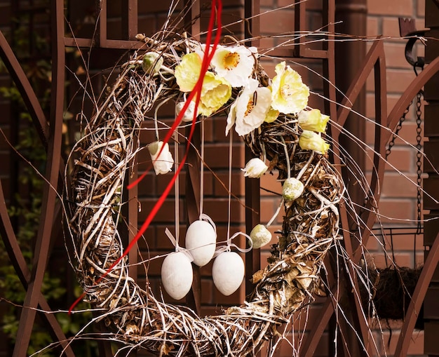 Drei Ostereier an Bändern in einem Osterkranz aus Weidenzweigen und Blumen, die an der Tür hängen