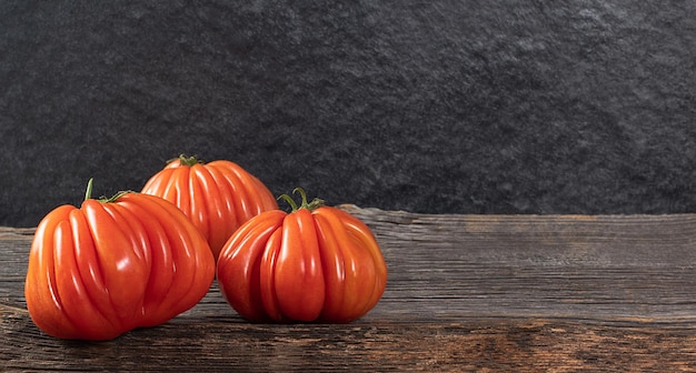 Drei Raf Coeur De Boeuf Tomaten auf einem rustikalen Konzept aus Holzhintergrund