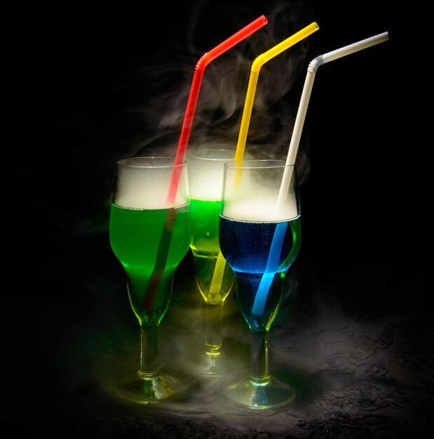 Drei rauchige Alkoholcocktails mit Trinkhalmen auf dunklem Hintergrund.