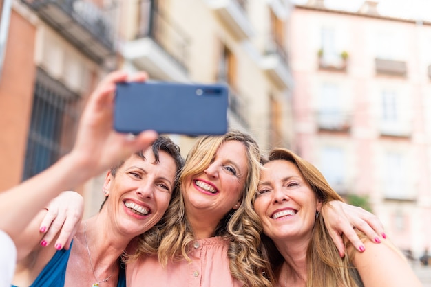 Foto drei reife freundinnen, die sich zusammen umarmen und ein selfie machen. freunde mittleren alters, die zeit miteinander teilen und spaß haben.