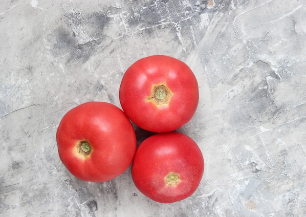 Drei reife Tomaten auf einem grauen Betonhintergrund.