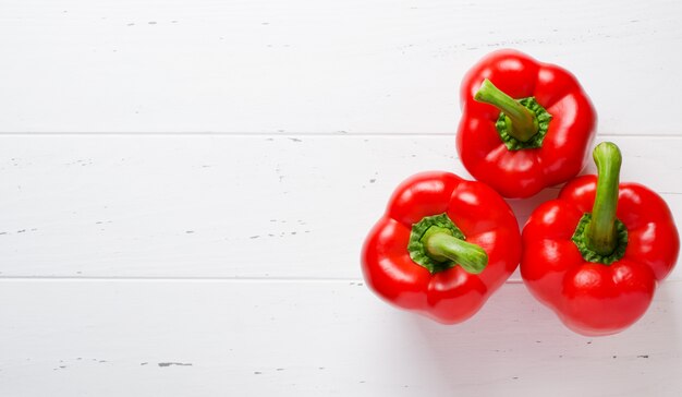 Drei rote reife Paprika. Weißer hölzerner Hintergrund.