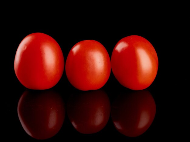 Drei rote Tomaten auf einem schwarzen glänzenden Hintergrund