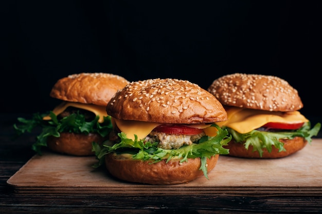 Drei saftige Hamburger mit Fleisch, Käse, Salat, Tomate auf einem Holzbrett