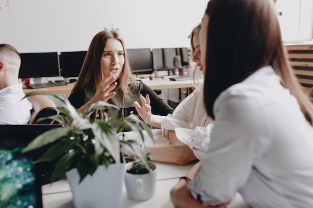 Drei schöne junge Frauen in Bürokleidung sitzen zusammen und sprechen im modernen Büro