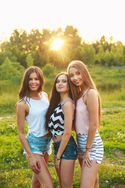 Drei schöne Mädchen gehen und lachen bei Sonnenuntergang im Park Freundschaftskonzept