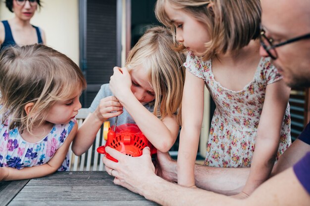 Drei schöne weibliche Kinder Außenterrasse Justierblasen Seifenmaschine von ihrem Vater geholfen