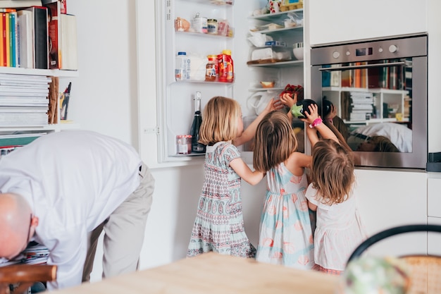 Drei schöne weibliche Kleinkind helfen ihrem Vater beim Auspacken von Lebensmitteln