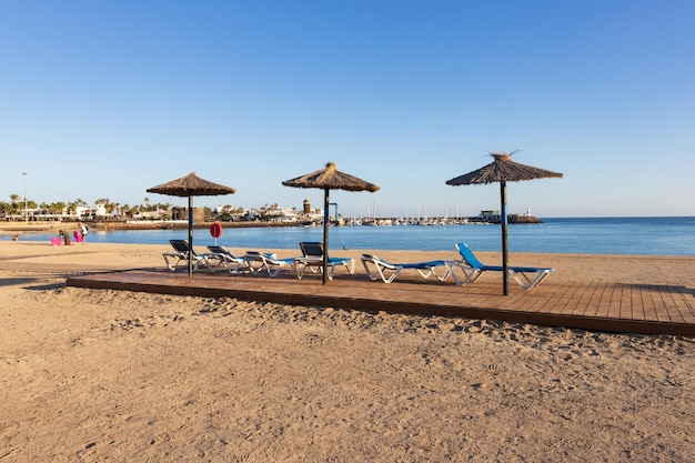 drei Sonnenschirme und Liegestühle an der Küste von Caleta de Fuste, Fuerteventura