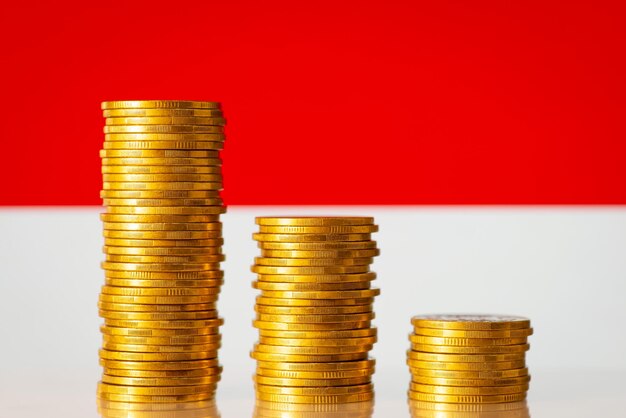 Drei Stapel Goldmünzen vom höchsten zum niedrigsten Wert mit der Flagge Indonesiens im Hintergrund. Konzept eines wirtschaftlichen Rückgangs mit negativer BIP-Rate in Indonesien