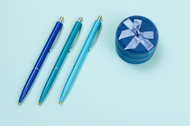 Drei Stifte und Geschenkbox auf blauem Grund. Ansicht von oben.