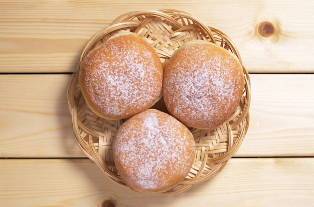 Drei süße Donuts in Korbteller auf Holztisch, Ansicht von oben