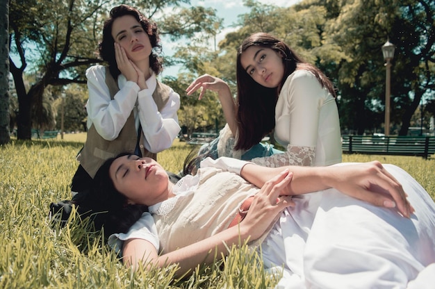Drei süße retro-lateinische argentinische Mädchen sitzen auf dem Gras und ruhen in einem öffentlichen Park