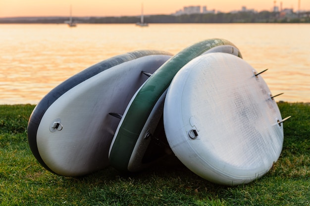 Drei Sup-Boards liegen auf dem Gras am Flusssee oder am Meer