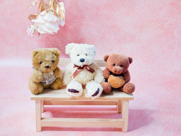 Drei Teddybären sitzen auf einer Holzbank mit rosa Hintergrund.