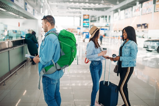 Drei Touristen mit Gepäck erhalten am Flughafen eine Bordkarte. Passagiere mit Gepäck im Flugterminal