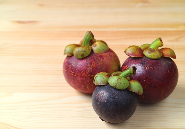 Drei verschiedene größen-und farbreife purpurrote mangostanfrucht-früchte auf dem holztisch