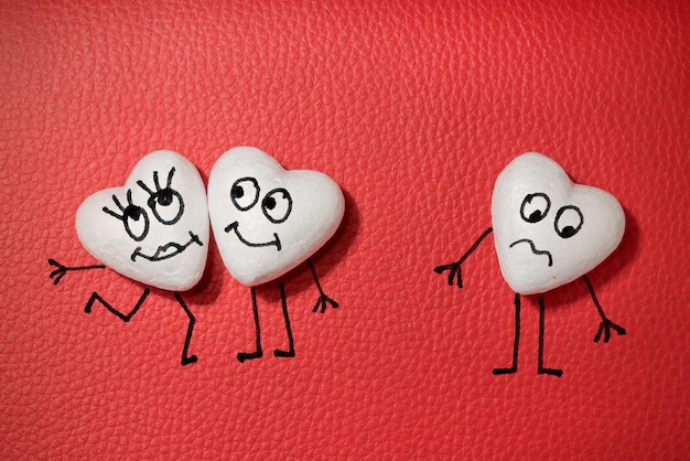 Drei weiße Herzen mit glücklichen und traurigen Gesichtern auf rotem Ledergrund