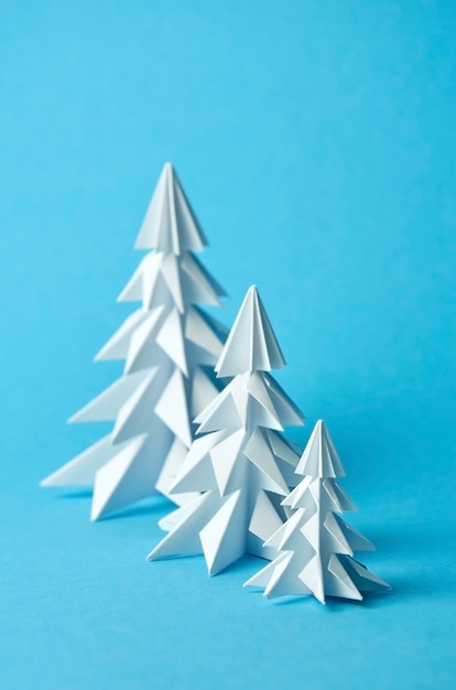 Drei weiße Papierorigami-Weihnachtsbäume auf Blau