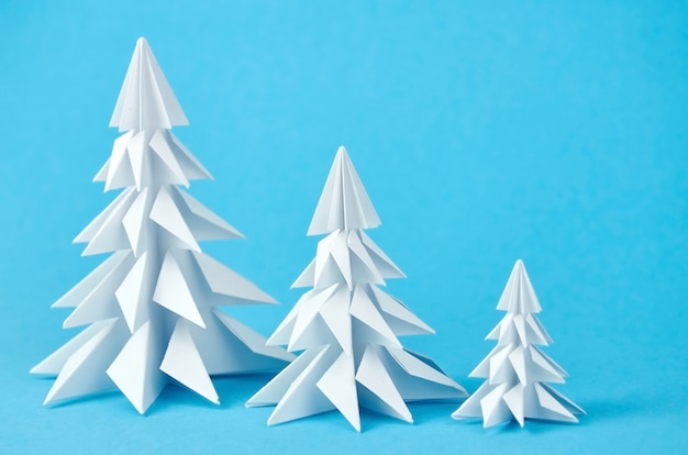 Drei weiße Papierorigami-Weihnachtsbäume auf Blau