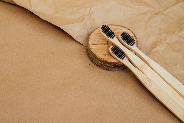 Drei Zahnbürsten aus natürlichem Bambus liegen auf einem Stück Holz vor einem Hintergrund aus braunem Kraftpapier. Ein nachhaltiger Lebensstil und ein plastikfreies Konzept, Bad Essentials.