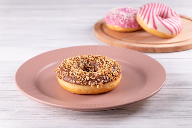 Drei zuckerbeschichtete Donuts liegen auf einer rosa Keramikplatte und einem Holzschneidebrett