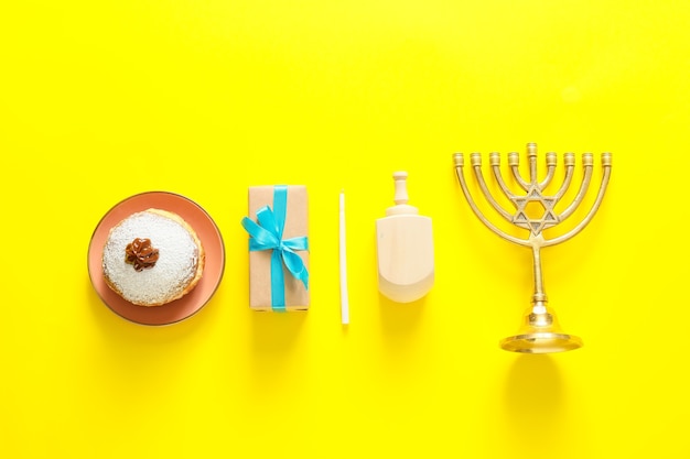 Dreidel und Donut für Chanukka mit Menora und Geschenk auf Farbhintergrund