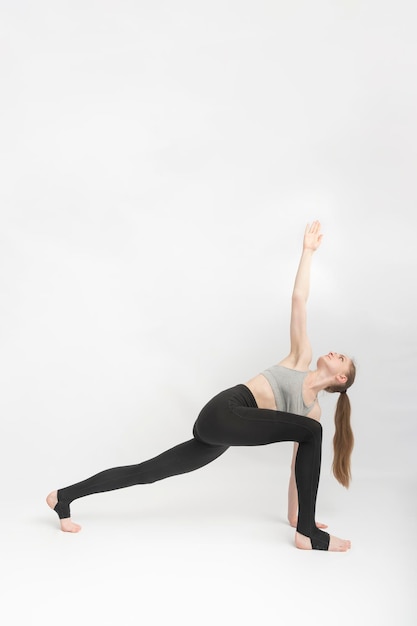 Dreieck-Pose. Trikonasana. Sportmädchen macht Yoga und führt Asanas auf weißem Hintergrund durch. Gymnastik, Stretching. Vertikaler Rahmen