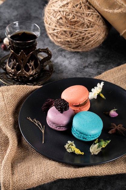 Dreifarbige französische Macarons auf einer schwarzen Untertasse und einem Glas Tee. Draufsicht