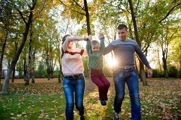 Dreiköpfige Familie genießen den Herbstpark, der Spaßlächeln hat