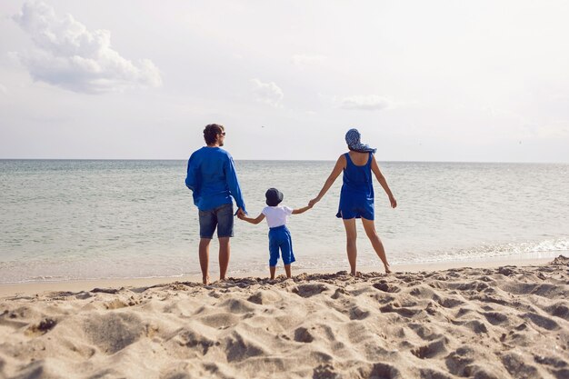 Dreiköpfige Familie in blauer Kleidung steht im Sommer im Urlaub an einem Sandstrand am Meer