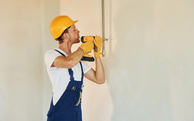 Drinnen im unfertigen Raum Junger Mann, der tagsüber in Uniform am Bau arbeitet