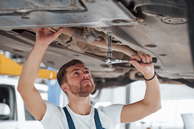 Drinnen in seiner Garage. Angestellter in blauer Uniform arbeitet im Automobilsalon.