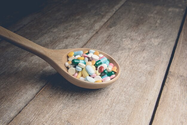 Droga la píldora en la cuchara de madera para su tratamiento su salud en fondo de madera