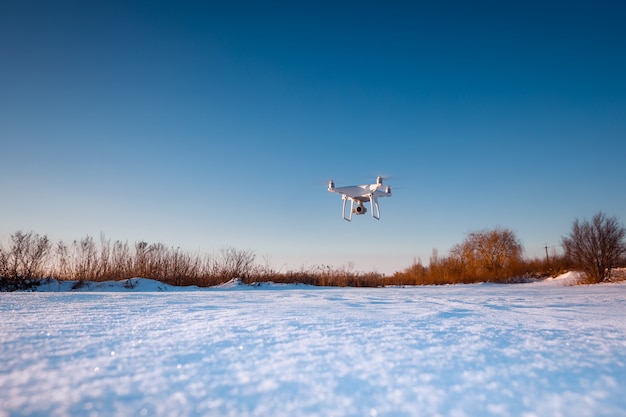 Drohne fliegt über Feld bedeckt mit Schnee an sonnigem Wintertag