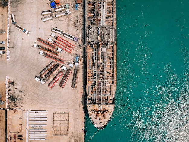 Drohnenansicht des Öltankers am Kai, der durch Gasleitungen Kraftstoff in zahlreiche Benzin-LKWs pumpt; Technologiekonzept.