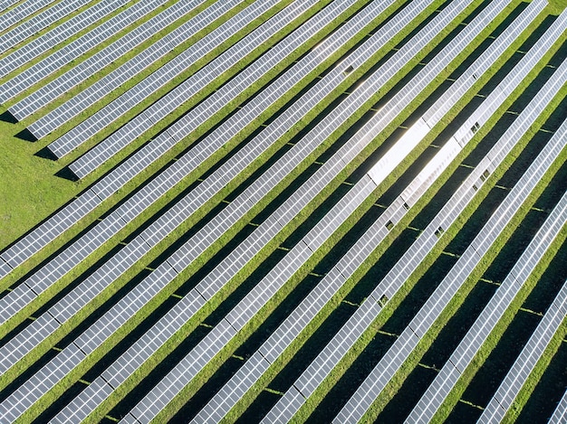 Drohnenansicht von oben nach unten auf riesige Gartenfelder und oben auf Sonnenkollektoren in einer Reihe. Erneuerbares Energiekonzept