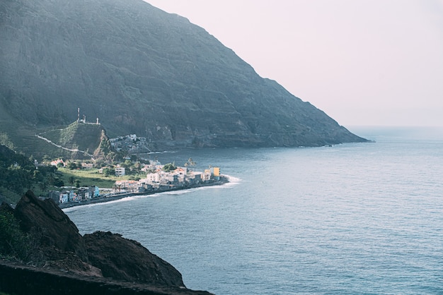 Drohnenblick auf das meer mit kleiner stadt in grünen bergen mit hohen felsigen gipfeln