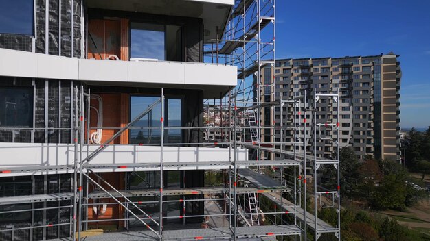 Drohnenflug entlang der Fassade eines modernen Wohnhauses im Bau, das von Gerüsten umgeben ist