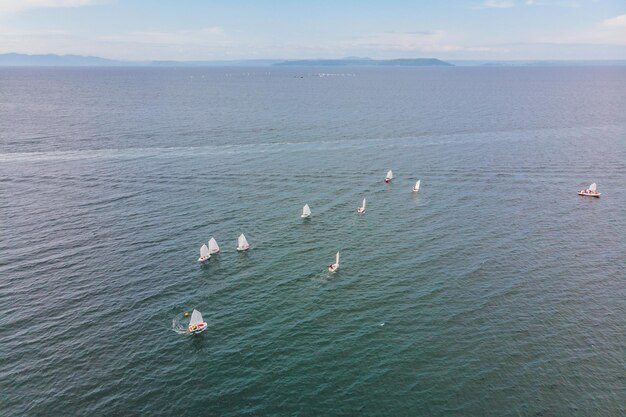 Drohnenfoto von jungen Teenagern auf kleinen Segelbooten, die an der Regatta im smaragdgrünen Mittelmeer teilnehmen.
