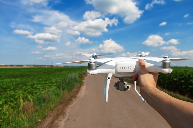 El drone blanco en manos del hombre aislado contra el fondo del campo verde