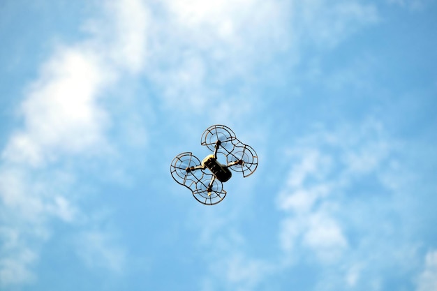 Drone de quatro motores com grade de proteção de hélices voando alto no céu azul com nuvens brancas calmas