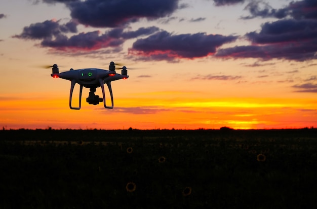 Drone está voando sobre o campo ao amanhecer. Fundo tecnológico moderno - silhueta de máquina voadora no céu vermelho brilhante do sol.