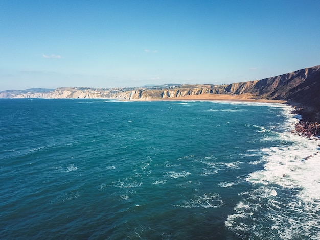 Drone vista aérea de los acantilados con muchas olas en una playa rocosa y arenosa