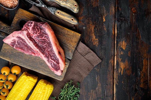 Dry-Aged rohes T-Bone- oder Porterhouse-Rindfleischsteak mit Kräutern und Salz, auf einem alten dunklen Holztisch