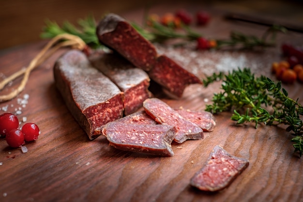 Dry-cured Salami geschnitten auf hölzernem Hintergrund mit Trauben und Kräutern