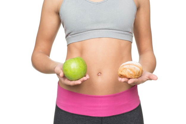 Foto du bist was du isst. kurzer schuss einer fitten frau mit getöntem körper, der einen apfel und ein croissant nahe ihrem flachen bauch hält