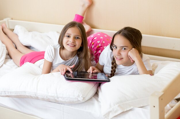 Duas adolescentes alegres deitadas na cama e usando o tablet